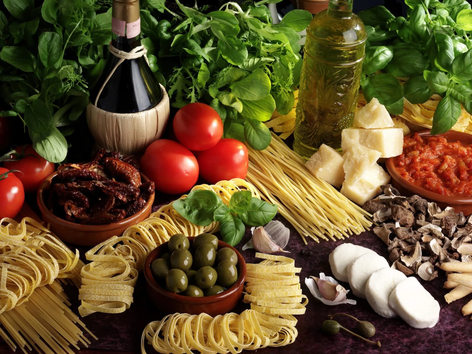 Pasta ingredients including dried pasta, tomatoes, Parmesan, mozzarella, olives, and herbs for Tuscan cuisine.