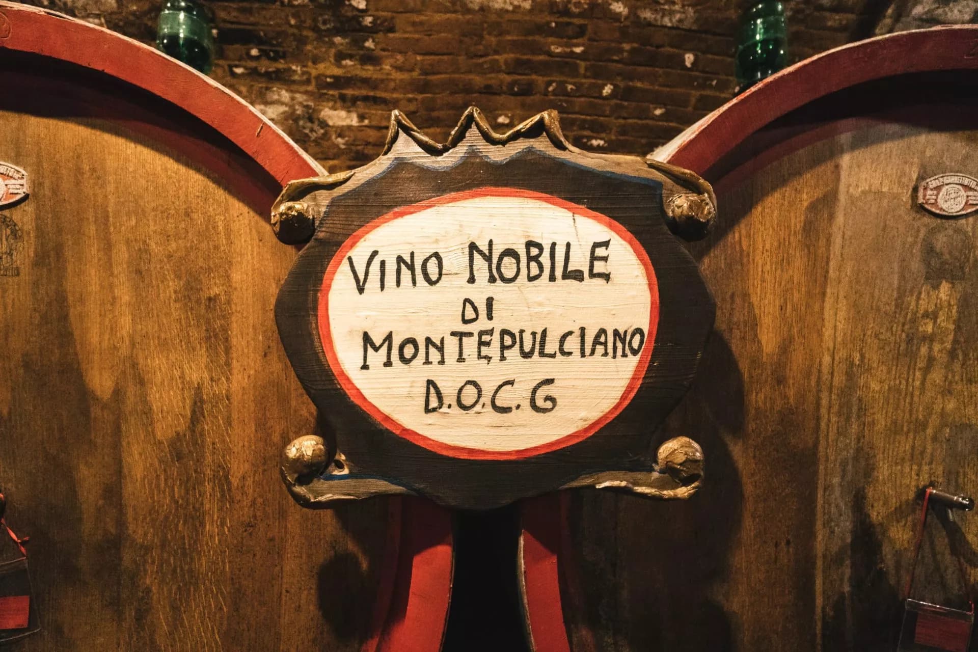 Hand-painted sign reading "Vino Nobile di Montepulciano D.O.C.G." on large wooden wine barrels.