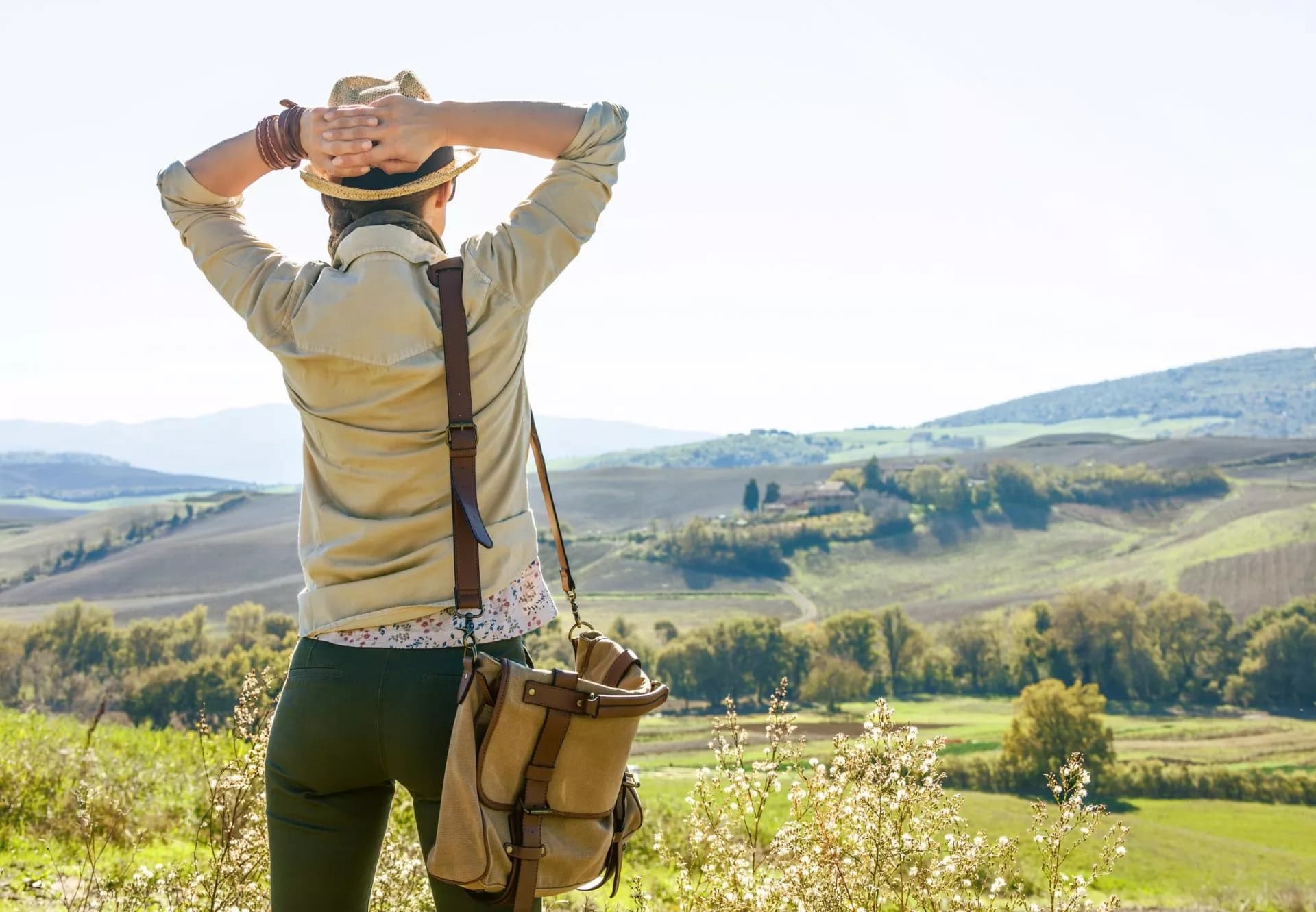 Hiker with straw hat observing rolling green hills and fields in Tuscany