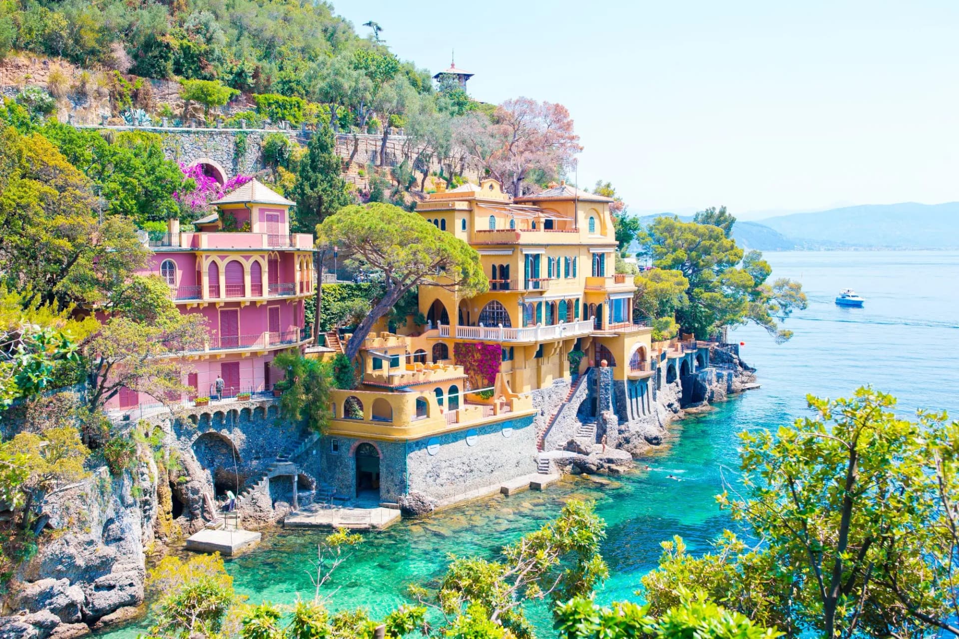 Colorful houses built into a cliff above turquoise water in Portofino with a boat on the sea.