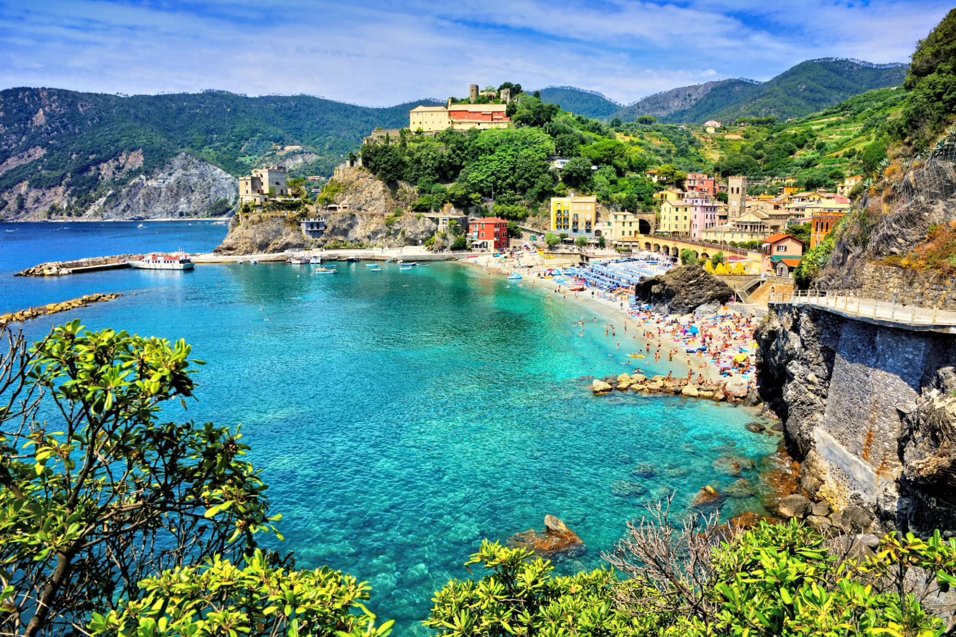 Beachgoers in Monterosso, Cinque Terre, with turquoise sea and colorful hillside village.