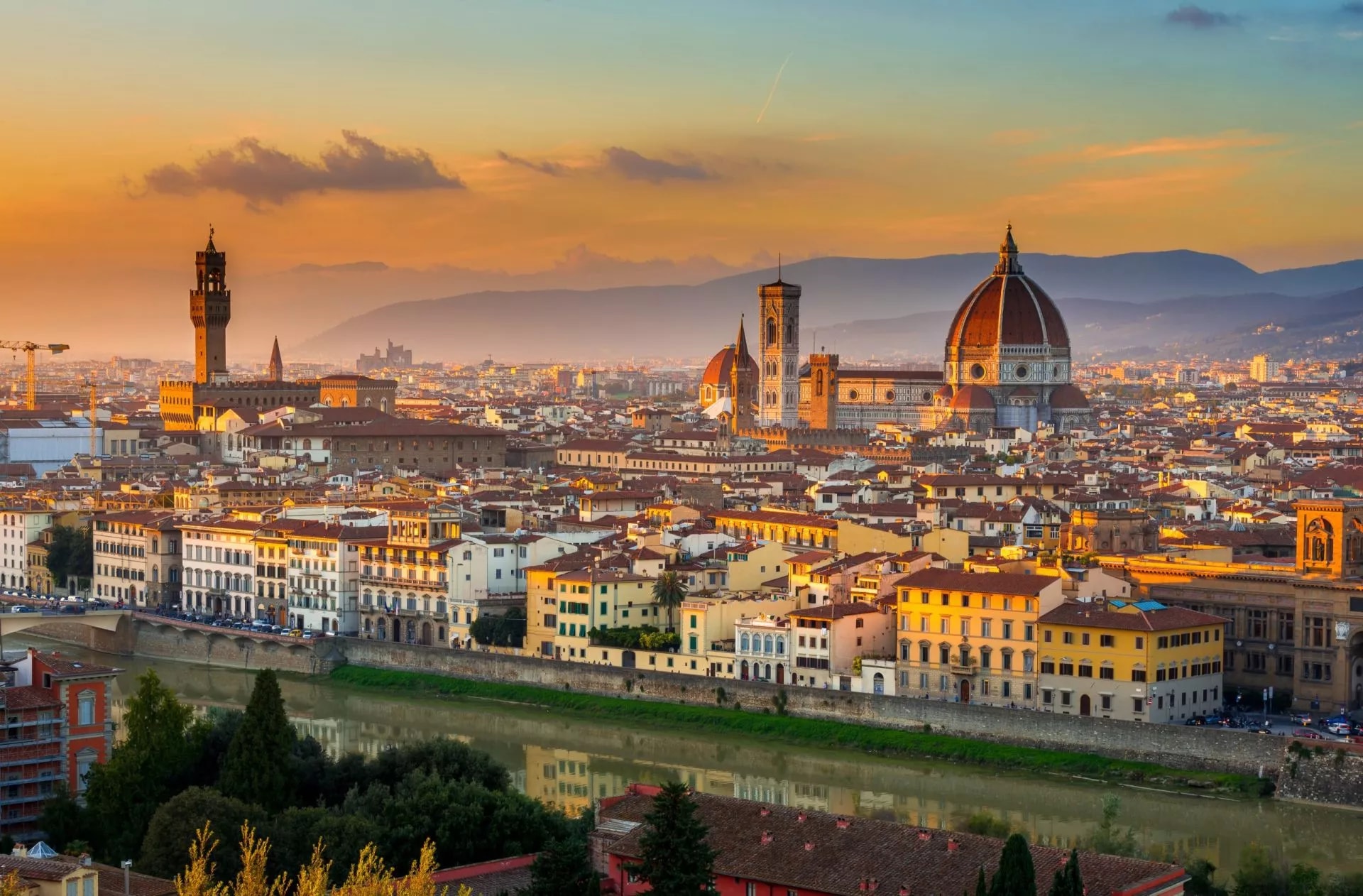 Florence cityscape at sunset with Duomo dome, Palazzo Vecchio tower, and Arno River.