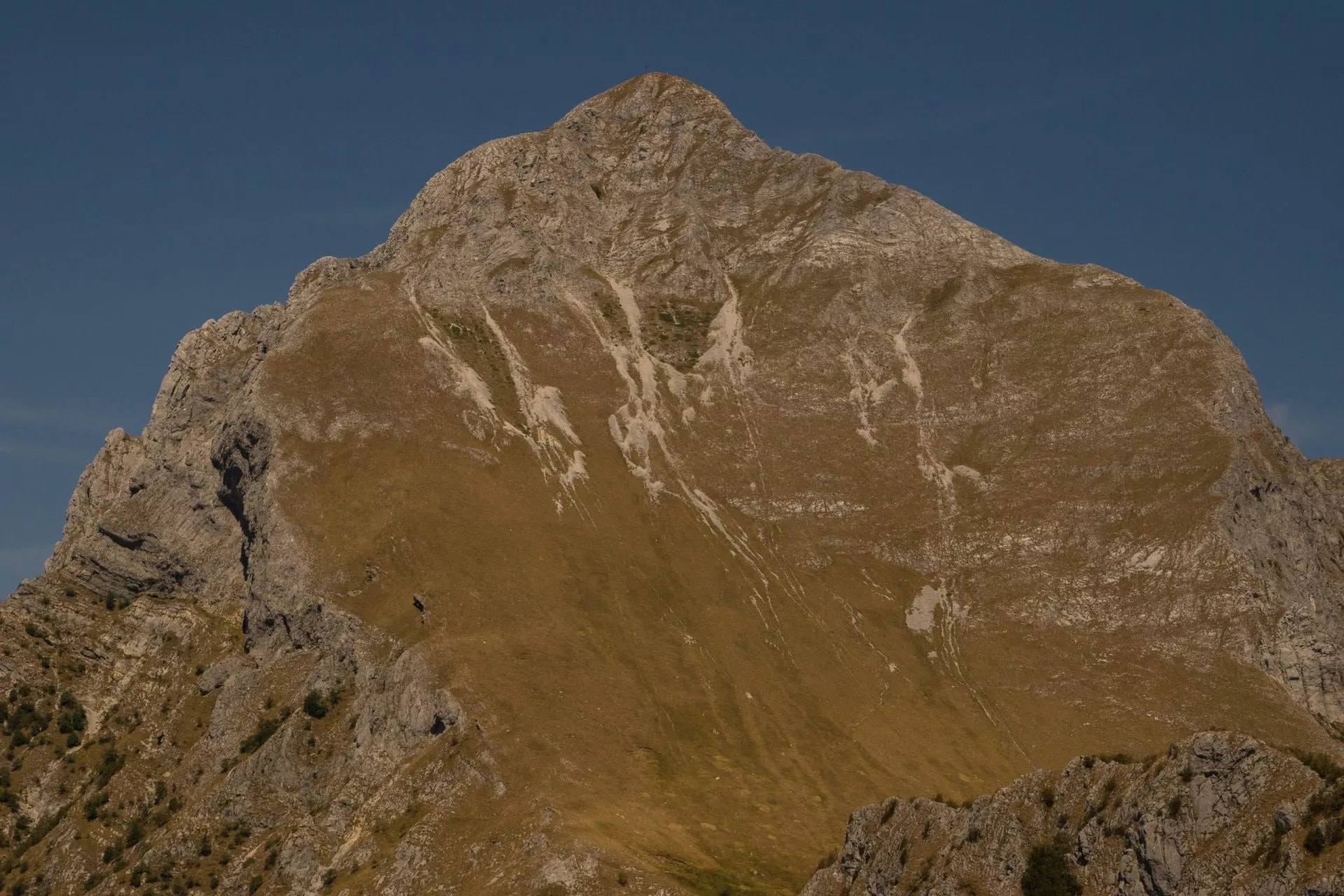 Rocky mountain peak with dry, golden slopes under a deep blue sky, Pania della Croce.