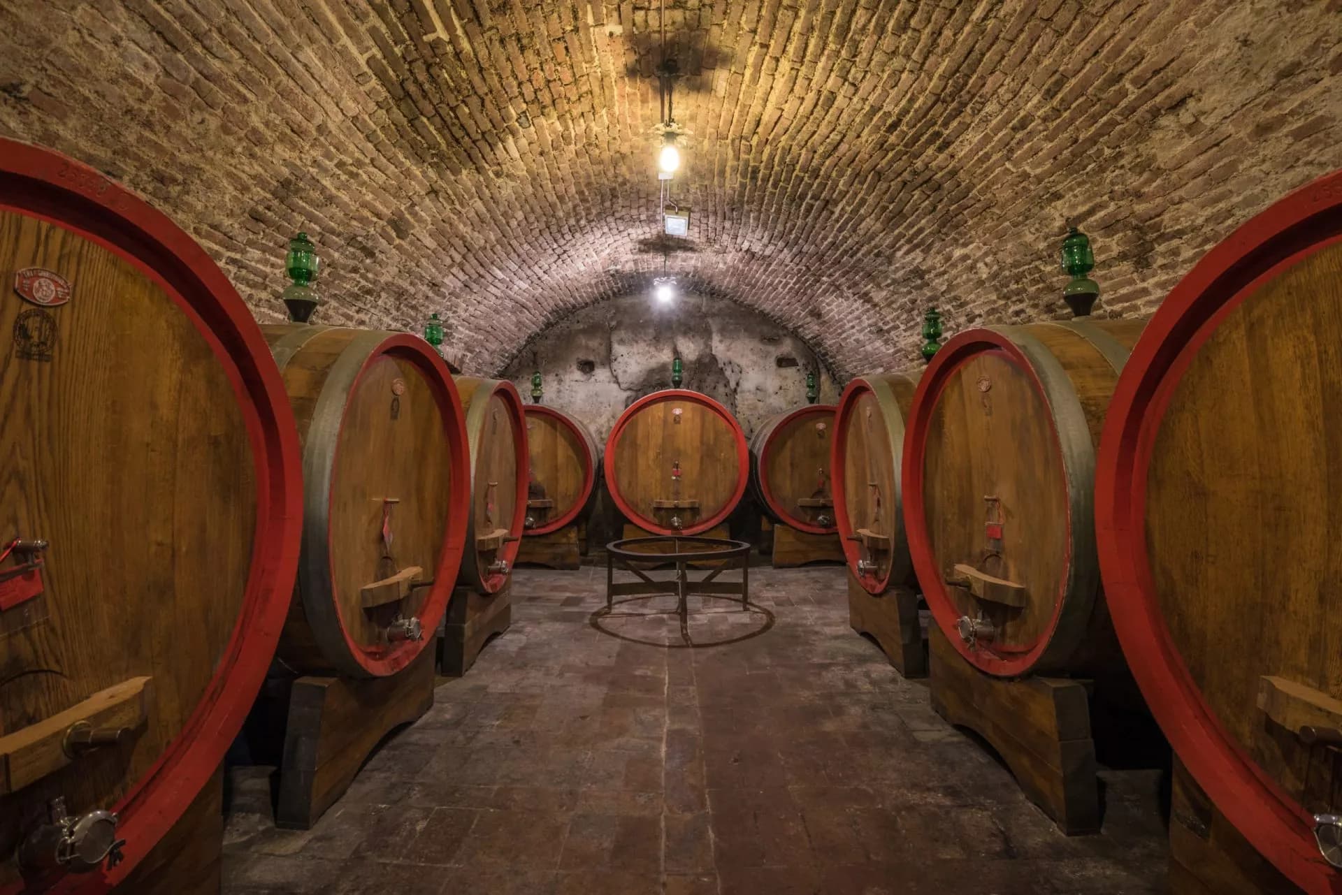 Large wooden wine barrels aging under a brick arched ceiling in a cellar.
