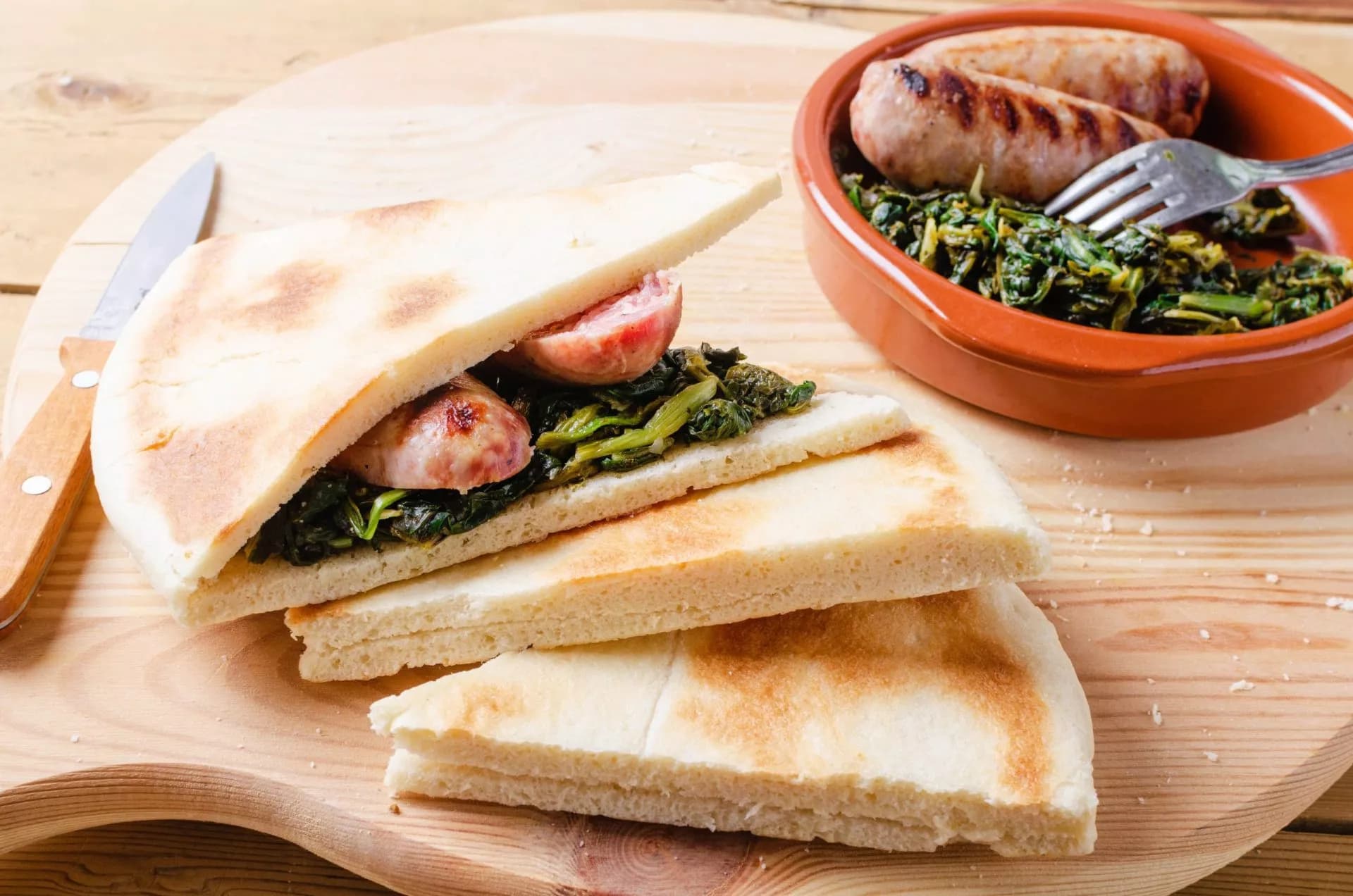 Flatbread sandwich with sausage and greens, served with grilled sausages on a wooden board