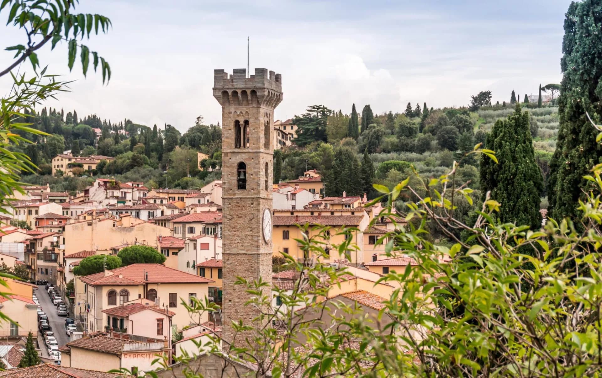 Stone clock tower overlooking Fiesole town with terracotta roofs and green hillsides.