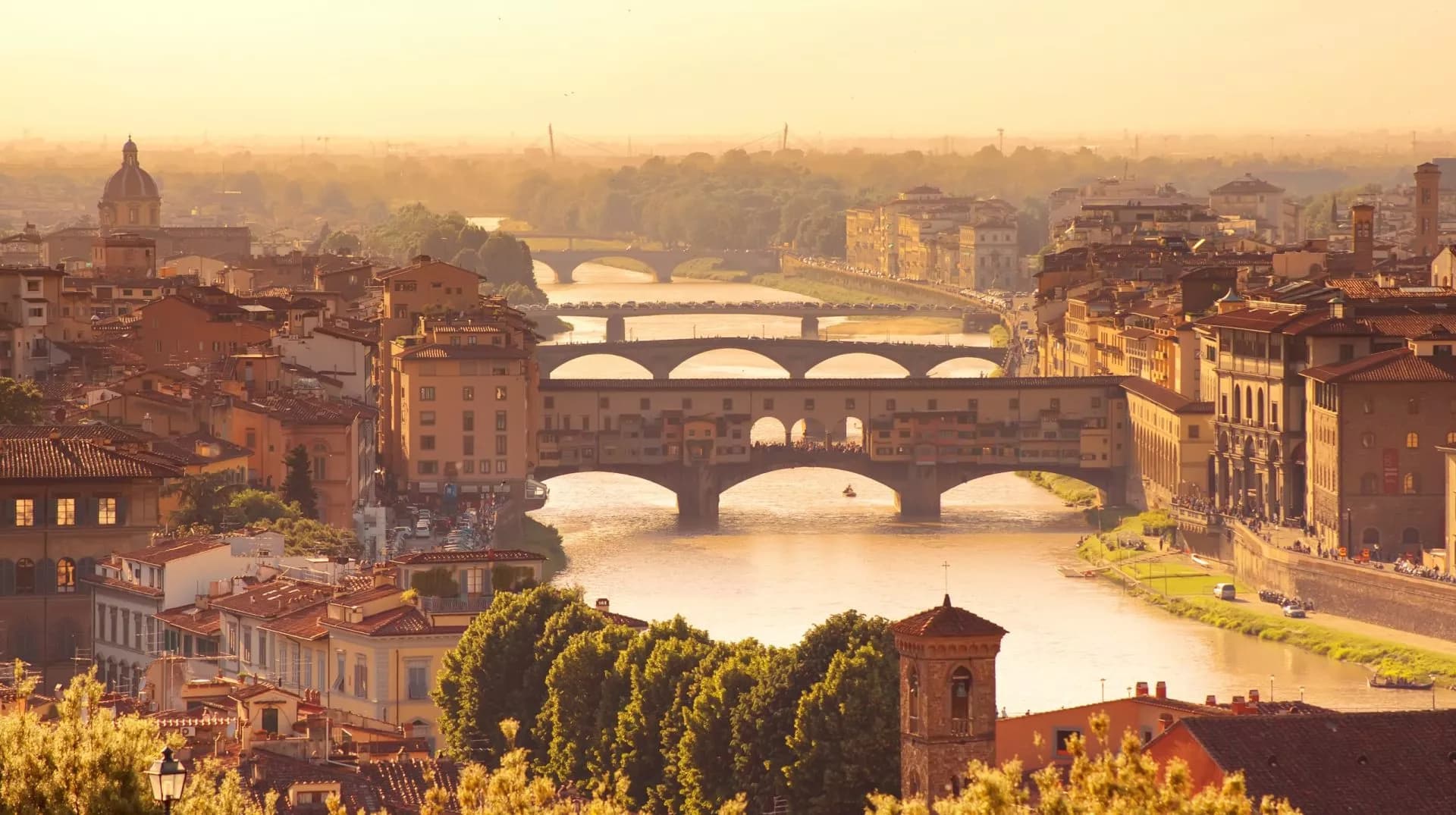 Ponte Vecchio bridge over the Arno River in Florence at sunset with hazy golden light.