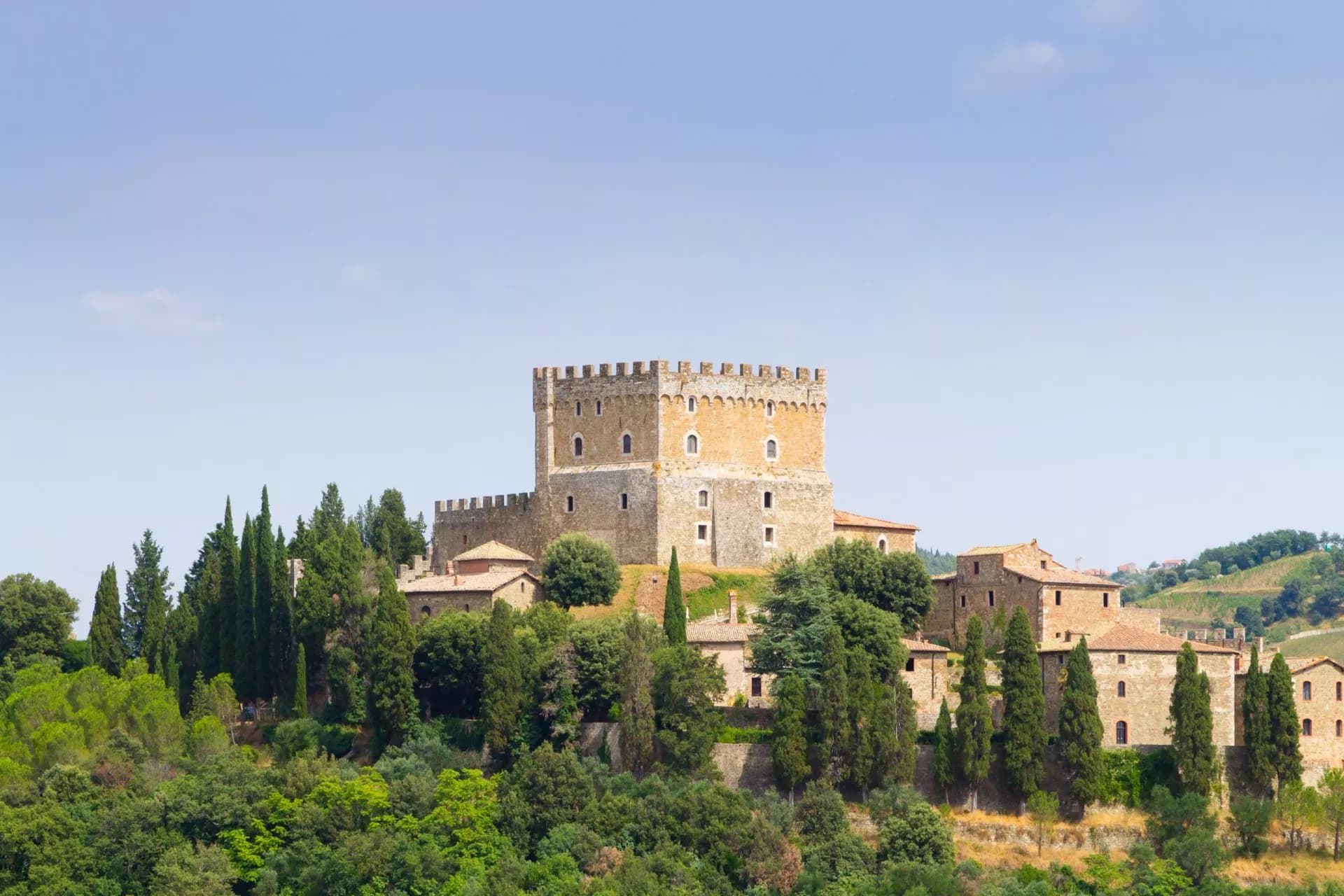 Ripa d'Orcia Castle perched above dense green trees under a clear blue sky.