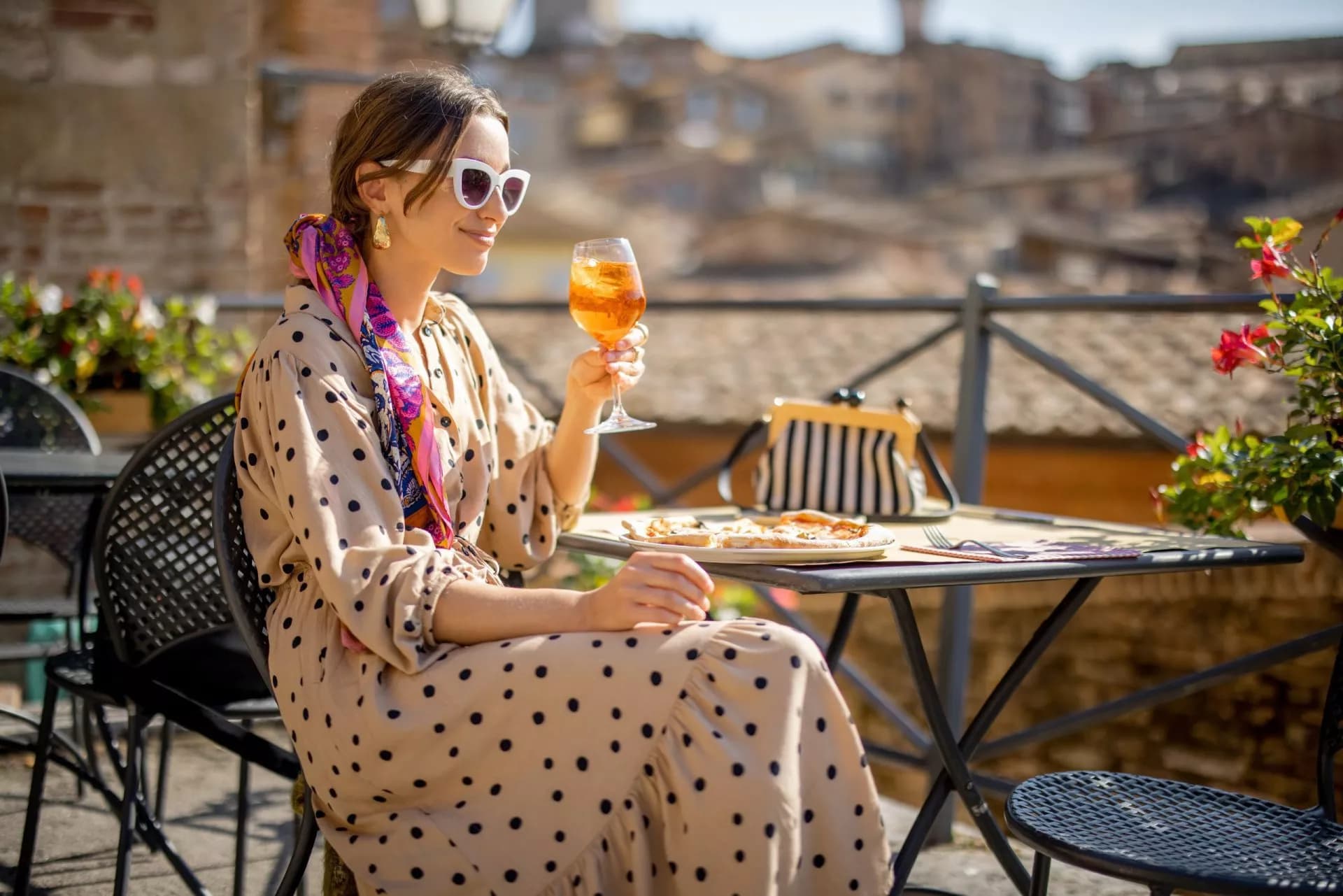 Woman enjoying an orange cocktail and pizza on a sunny outdoor terrace in Tuscany.
