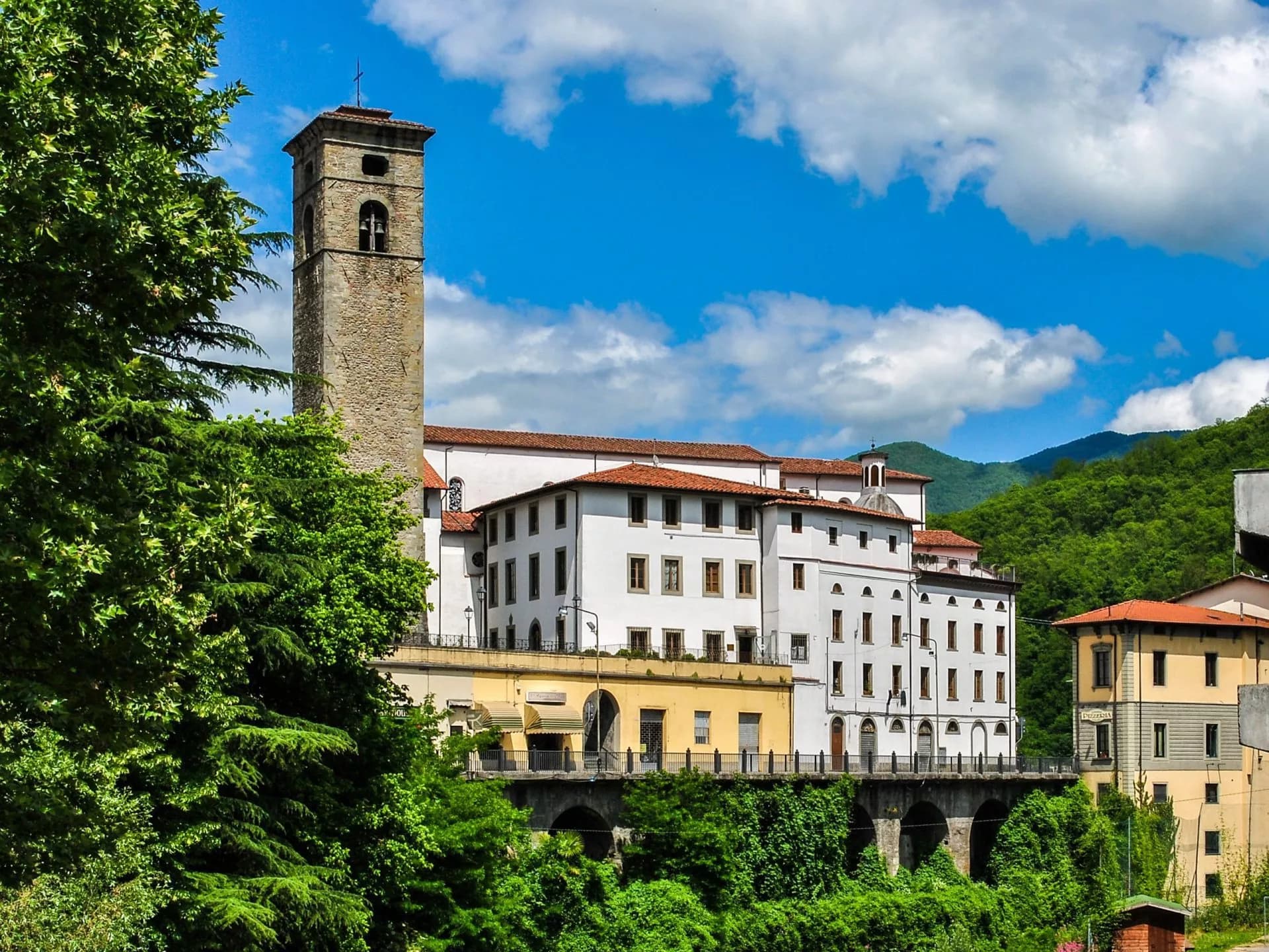 Stone medieval tower and white buildings above green hills under a blue sky in Castelnuovo.