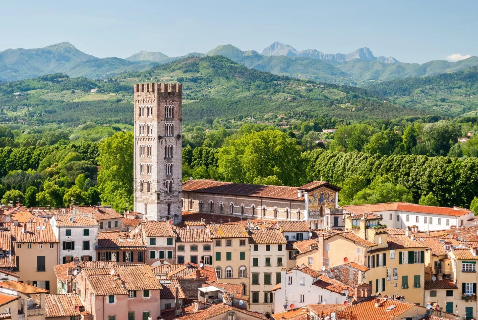 Lucca cityscape with medieval tower, terracotta roofs, and green hills under mountains
