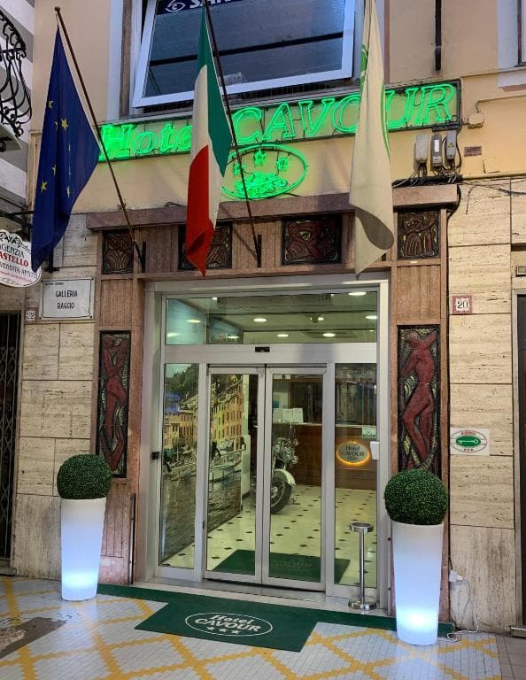 Hotel Cavour entrance with Italian and EU flags, green neon sign, and illuminated planters.
